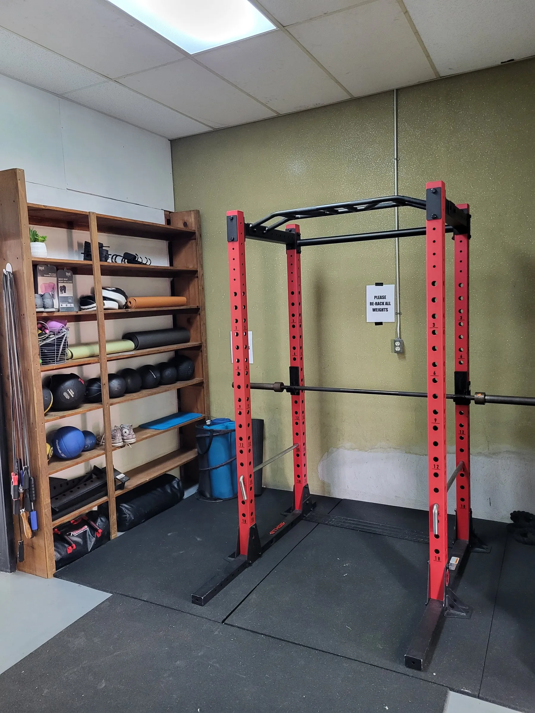 A red power rack beside shelves of kettlebells and medicine balls